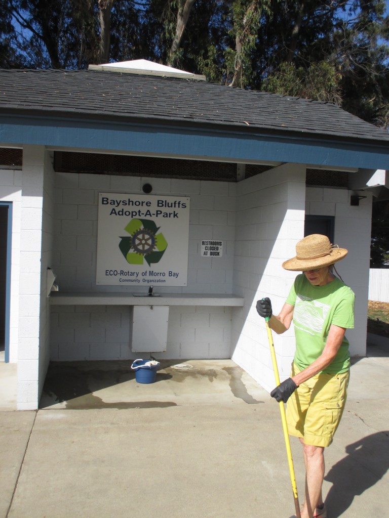 Charlotte sweeps the sidewalk near the Eco Rotary Club’s Adopt-A-Park sign. 