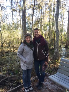 Communications and Outreach Coordinator Rachel Pass (left) and Executive Director Lexie Bell (right) stand in front of a bald cypress swamp in Jean Lafitte National Park outside of New Orleans, Louisiana.