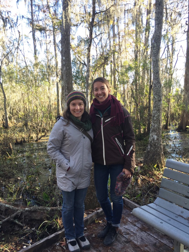Communications and Outreach Coordinator Rachel Pass (left) and Executive Director Lexie Bell (right) stand in front of a bald cypress swamp in Jean Lafitte National Park outside of New Orleans, Louisiana.