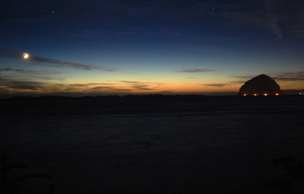 Morro Bay beneath a setting sun and a rising moon.