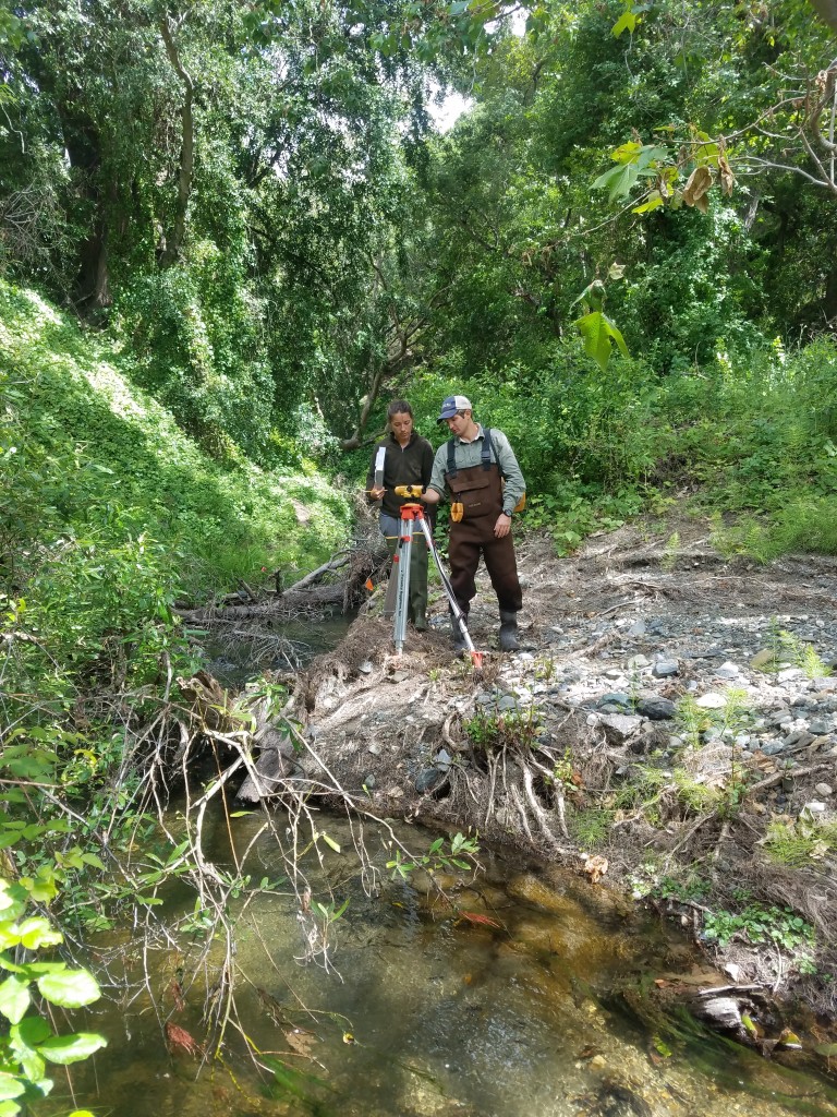 Evan, our Field Technician, shows a volunteer how to use a device called an auto level to measure the slope of the stream. An auto level is essentially a telescope that allows us to measure the elevations of our transects (the set areas where we are collecting data) from a fixed location along the stream. 