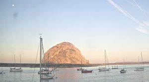 The moon is in the top left corner above Morro Rock and the sunset.