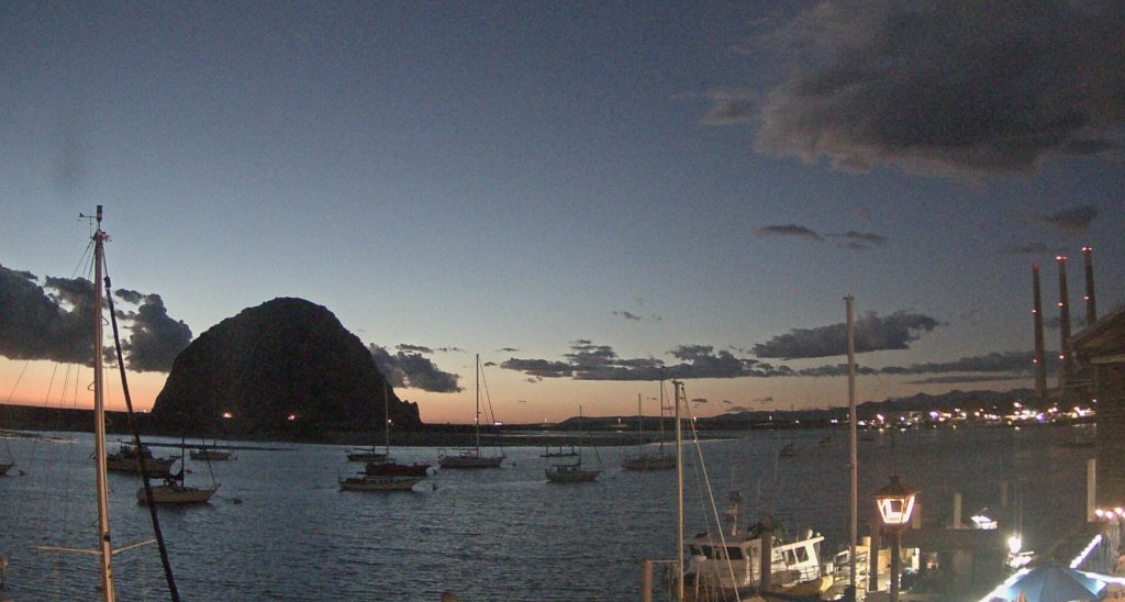 Lights on the Embarcadero turn on as the sun casts an orange glow behind Morro Rock. 