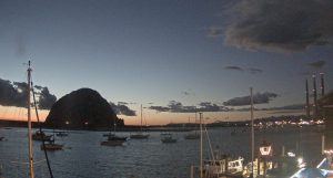 Lights on the Embarcadero turn on as the sun casts an orange glow behind Morro Rock.