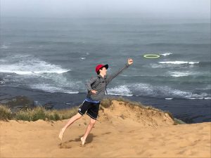 Eli Hague, poetry contest winner leaps to catch a frisbee near the ocean.