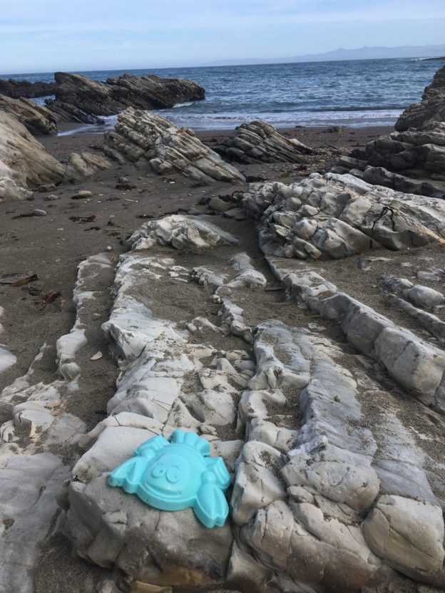 A plastic sand toy left on rocks at the beach.